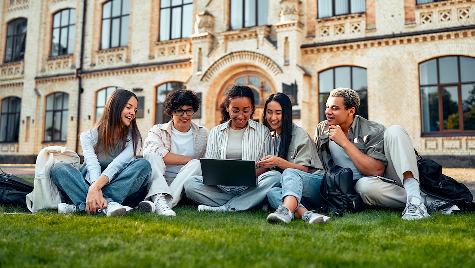 Students sitting on the grass, looking at a laptop